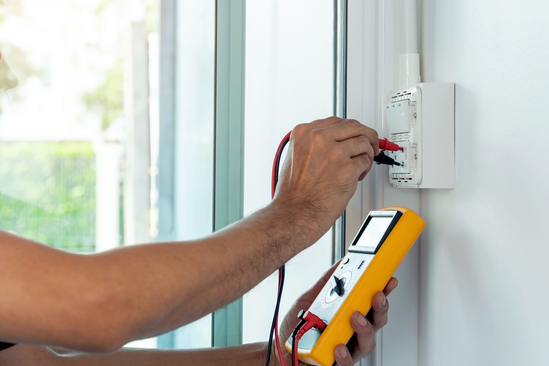 Electrician using a digital meter to measure the voltage at a wall socket.