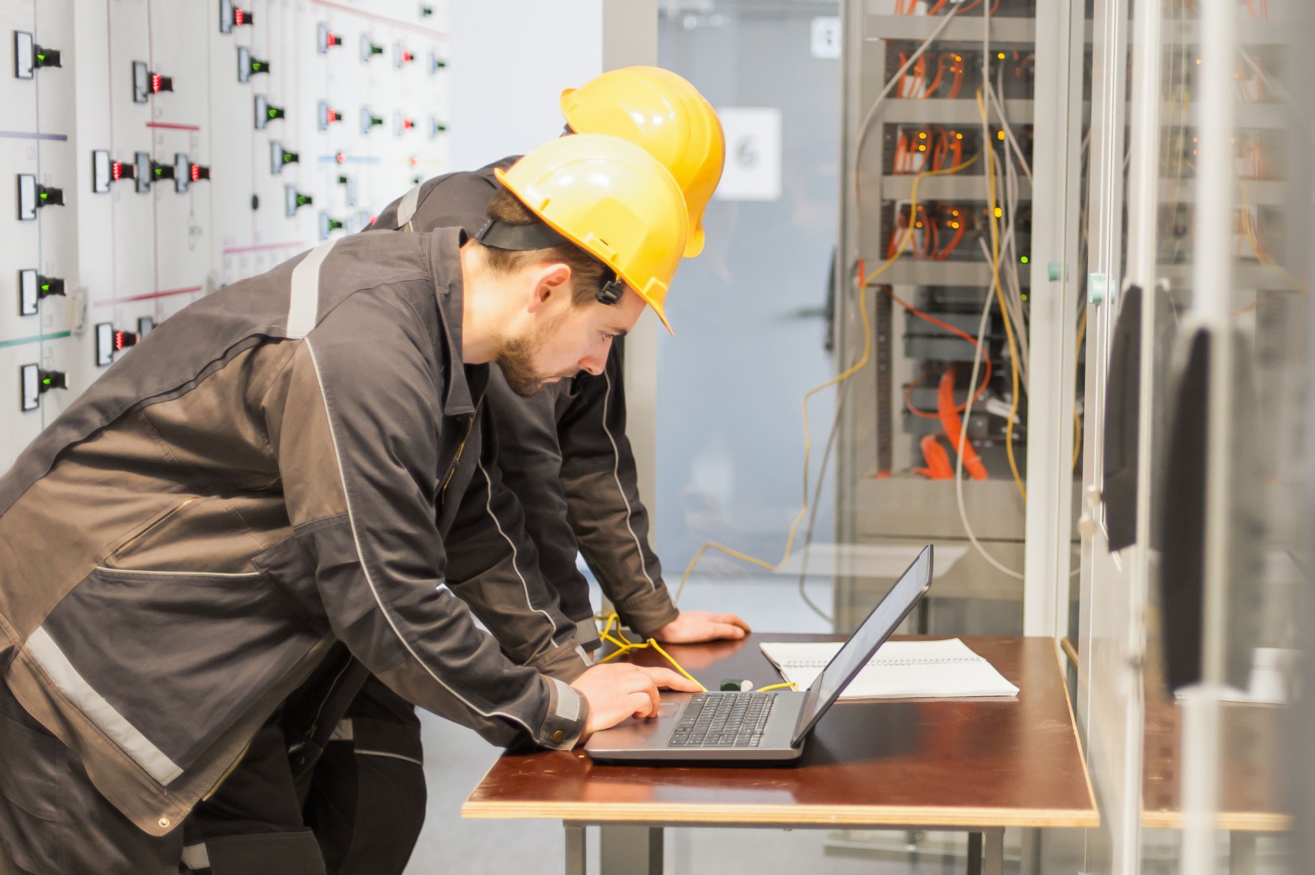 Two maintenance engineers inspect relay protection system with laptop comp